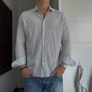 Ljusgrå skjorta från Massimo Dutti M - Snygg ljusgrå skjorta från Massimo Dutti i storlek M. Skjortan har klassisk krage, knäppning framtill och långa ärmar. Tillverkad i ett mjukt bomullstyg som känns skönt mot huden. Perfekt till jeans för en clean och stilren look.