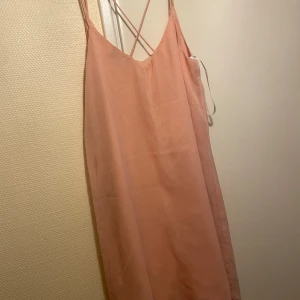 Ljusrosa sommarklänning Vero Moda - Säljer en ljusrosa klänning från Vero Moda i storlek M. Klänningen är ärmlös med tunna axelband som korsas i ryggen och har en lös, rak passform. Perfekt för varma dagar och enkel att styla med accessoarer.