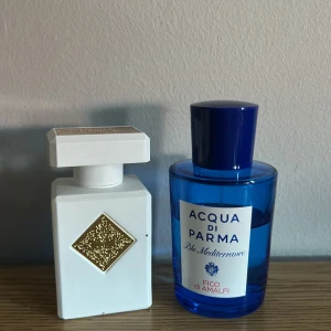 Acqua di Parma & Parfymflaska - Två exklusiva parfymer: en Acqua di Parma Blu Mediterraneo Fico di Amalfi i en klarblå rund flaska med blått lock och vit etikett, samt en vit fyrkantig parfymflaska med guldfärgad dekor och lock. Perfekt för dig som gillar lyxiga dofter.