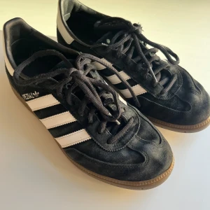Adidas Spezial svarta sneakers i mocka - Svarta Adidas Spezial sneakers i mjuk mocka med klassiska vita ränder på sidorna och gummisula. Skorna har snörning och en retro vibe som passar perfekt till streetwear. Ikonisk Spezial-logga i vitt på sidan. Runda tår och låg profil.