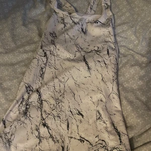 Vit träningstopp med marmormönster - Snygg vit träningstopp med svart marmormönster och smala axelband. Toppen är ärmlös och har en tight passform, perfekt för dig som gillar en modern och trendig look.