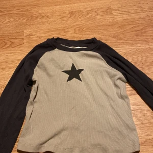  långärmad tröja med stjärna H&M - Snygg långärmad tröja från H&M i beige med mörkgråa ärmar och en mörkgrå stjärna på bröstet. Tröjan är lite croppad. Använt väldigt några gånger.