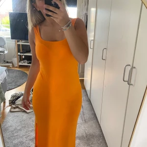 Orange långklänning med slits - Snygg orange långklänning med breda axelband och rundad urringning. Klänningen är figurnära och har en hög slits på ena sidan som ger en cool touch. Perfekt för varma dagar när du vill sticka ut med färg.