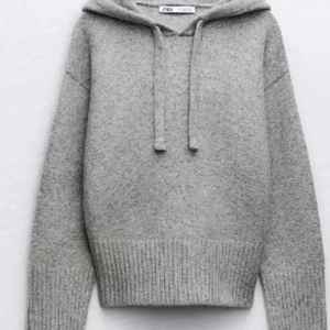 Grå stickad hoodie från Zara - Mysig grå stickad hoodie från Zara med huva och snörning. Tröjan har ribbade muddar och lång ärm, perfekt för kyliga dagar. Enkel och stilren design som passar till det mesta.