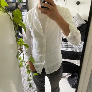 Vit linneskjorta från Polo Ralph Lauren - Fräsch vit henley-skjorta från Polo Ralph Lauren i slim fit. Skjortan är tillverkad i svalt linne, har långa ärmar, knappar framtill och klassisk broderad logga på bröstet. Perfekt för en clean och stilren look.