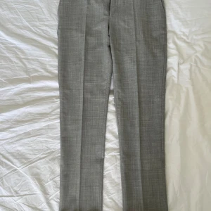 Suitsupply ullbyxor i storlek 48/M - Product Code B7040 Material Pure S120's Tropical Wool Composition 100% Wool Fabric Code 540.901/1 Color Light Grey Woven by Vitale Barberis Canonico, Italy Care Instructions Dry Clean Only  Slim through the hip and thigh, with a slim straight leg Mid-rise trousers Flat front Belt loops Slanted side pockets Jetted button back pockets After-dinner split Turn up