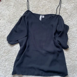 Svart linnetopp från ASOS - Svart linnetopp från ASOS med tunna axelband och v-ringning. Toppen har en flowy passform och korta, lösa ärmar som ger en cool och avslappnad vibe. Perfekt att styla med jeans eller kjol för en trendig look.