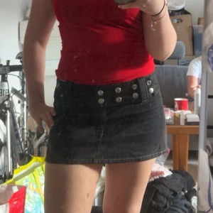 Svart minikjol från diesel med inbyggd bälte  - Svart kortkjol i jeansmaterial med bred midja, silverfärgade nitar och tillhörande bälte med öljett-detaljer. Snygga kontrastsömmar och fickor bak. Perfekt för dig som gillar edgy och trendig stil. Har vanligtvis 36 i byxor o kjolar och denna sitter bra!