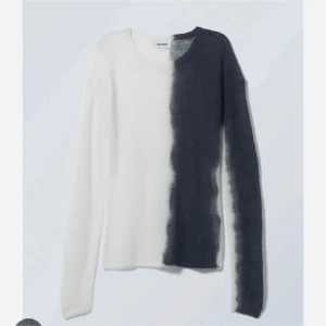 Weekday stickad tvåfärgad tröja - Säljer en tunn stickad tröja från Weekday med unik design – ena halvan är vit och andra halvan är mörkgrå, med en cool suddig kant mellan färgerna. Tröjan har rund hals och långa ärmar, sitter tight och är perfekt för dig som gillar statement-plagg.