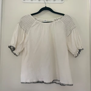 Vit blus med svarta detaljer från Zara - Luftig vit blus från Zara med svarta broderade detaljer på axlar, ärmslut och nederkant.