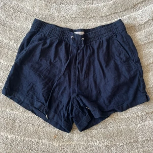 Mörkblå linneshorts från H&M - Snygga mörkblå shorts från H&M i luftig linnemix. De har elastisk midja med snörning, sidfickor och två bakfickor. Perfekta för varma dagar när du vill ha en chill och stilren look.