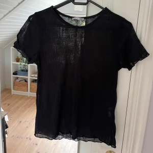 Svart transparent topp från Zara - Säljer en svart, tunn och transparent topp från Zara. Modellen har korta ärmar och rund halsringning. Tyget är lätt och luftig, perfekt för lager-på-lager eller att styla med ett snyggt linne under. Enkel och stilren design som passar till många looks.
