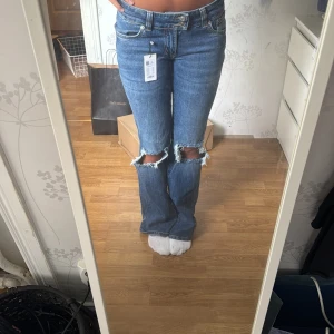 Blå bootcut jeans med slitna knän - Säljer ett par blå bootcut jeans med slitna hål över båda knäna. Jeansen har klassisk femficksdesign, låg midja och är tillverkade i jeansmaterial. Perfekta för dig som gillar en avslappnad och trendig look. Helt nya med prislapp kvar❤️
