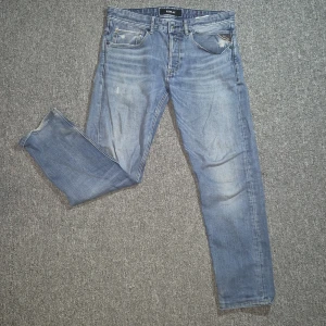 Replay ljusblå jeans straight fit - Snygga ljusblå jeans från Replay med klassisk femficksdesign och raka ben. Jeansen har slitna detaljer och diskreta slitningar för en cool, avslappnad look. Tillverkade i mjukt denimtyg med normal passform och medel midja.
