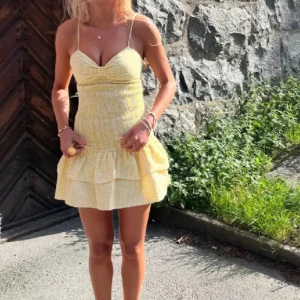 Gul kort volangklänning med smock - HELT NY. Supersöt gul kort klänning med smala axelband, smockad överdel och volangkjol. (Inte mina bilder)