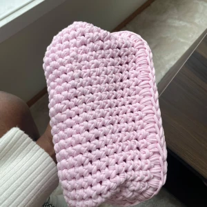 Handgjord rosa stickad kuvertväska - Supersöt handgjord kuvertväska i ljusrosa, virkad i tjockt garn med rektangulär form. Perfekt att bära småsaker i och ger en unik touch till din outfit. Väskan är mjuk och har en enkel öppning upptill.