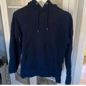 Mörkblå hoodie - Enkel och stilren mörkblå hoodie från SOC i storlek XS. Tröjan har huva med snörning, känguruficka framtill och är tillverkad i mjuk bomullsmix. Perfekt för chill dagar eller när du vill ha en avslappnad look.
