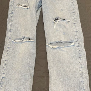 Ljusblå ripped jeans från g perfect jeans - Säljer ett par ljusblå jeans från g perfect jeans med snygga slitningar och hål på båda benen. Klassisk femficksmodell med dragkedja och knapp. Jeansen har en rak passform och är perfekta för en avslappnad streetstil.