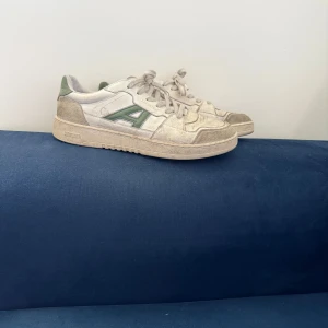 Arigato sneakers i vitt och grönt - Snygga sneakers från Arigato i vitt med gröna detaljer och en stor grön A-logga på sidan. Skorna har snörning, rund tå och är tillverkade i skinn och mocka. Perfekta för dig som gillar en clean och sportig look. Lite skitiga men tvättar dom såklart vid försäljning! Annars är det bara att höra av dig vid funderingar!😉