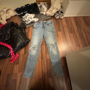 Ljusblå ripped jeans från 157 - Säljer ett par ljusblå jeans från 157 med hög midja och skinny fit. Jeansen har slitna detaljer och hål på båda knäna för en cool, trendig look. Klassisk femficksmodell och tillverkade i stretchig denim för skön passform.