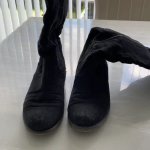 Svarta mockastövlar med dragkedja - Svarta stövlar i mocka med rund tå och dragkedja längs sidan. Snyggt höga och perfekta till både kjol och jeans. Sula med stjärnmönster för extra grepp. Klassisk och stilren look som funkar året runt.