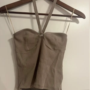 Beige ribbad korsettopp Gina Tricot - Supersnygg beige halter topp från Gina Tricot i ribbat material. Figurnära passform och lätt vadderade kupor för extra stöd. 