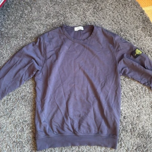 Mörkblå Stone Island sweatshirt - Snygg mörkblå sweatshirt från Stone Island Junior med klassisk rund hals och ikonisk logga på vänster ärm. Tröjan är i mjuk bomull och har långa ärmar med ribbade muddar. Perfekt för dig som gillar streetwear och vill ha en clean look.