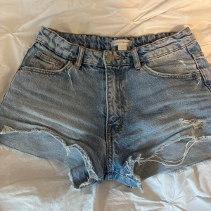 Blå jeansshorts från Gina Tricot - Snygga lågmidjade blå jeansshorts från Gina Tricot x Izaandelle med råa, fransiga kanter och slitna detaljer. Klassisk femficksmodell med knapp och dragkedja framtill. Perfekta för varma dagar och en avslappnad look. Storlek 152 men passar även xs ❤️❤️🫶