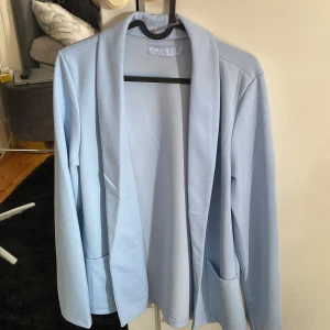 Ljusblå kavaj med fickor - Snygg ljusblå kavaj från Fanny Blomme med lång ärm och två stora fickor framtill. Enkel och stilren design utan knappar, perfekt att slänga på sig över en t-shirt eller hoodie. Skön och mjuk känsla i materialet.