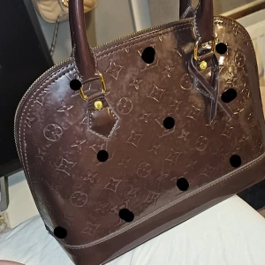 Brun lack väska - Brun elegant design väska i brun lack färg med monogram och guld detaljer. Aldrig använd och den förtjänar att bli använd och älskad för dens fina skönhet och utseende. Kolla gärna in min profil.