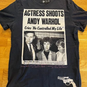 Andy Warhol t-shirt Pepe Jeans London - Svart t-shirt från Andy Warhol x Pepe Jeans London med stor tidningsinspirerad print framtill. T-shirten har korta ärmar, rund hals och är gjord i mjuk bomull. Unik design med text och bild, samt liten revolverdetalj längst ner på framsidan.