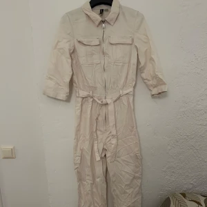 Vit jumpsuit från H&M  - Vit jumpsuit från H&M Divided med dragkedja framtill, knytskärp i midjan och fickor på bröstet och benen. En liten fläck på ena benet. Storlek 34
