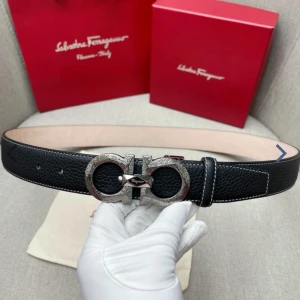 Svart skärp från Salvatore Ferragamo - Snyggt svart bälte från Salvatore Ferragamo i äkta skinn med grov textur och vit kontrastsöm längs kanterna. Spännet är i silverfärgad metall med ikonisk dubbel Gancini-design och graverad logga. Perfekt accessoar för att lyfta din outfit.