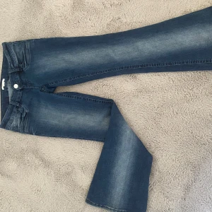 Blå bootcut jeans med slitningar - Snygga blå bootcut jeans med lätt slitning och tvättade detaljer. Klassisk femficksmodell med knapp och dragkedja framtill. Jeansen har en något utsvängd passform nertill och är tillverkade i mjukt denimtyg.