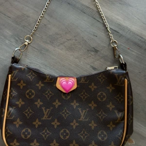  axelväska med monogram - Snygg axelväska från L  i klassiskt brunt monogrammönster med guldiga kedjedetaljer. Väskan har dragkedja upptill och detaljer i beige skinn. Perfekt storlek för det viktigaste och en ikonisk accessoar till din outfit.