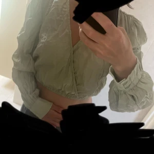 Ljusgrön omlottopp med puffärm - Superfin ljusgrön omlottopp från NA-KD med croppad passform och långa puffärmar. Toppen har v-ringning och resår i midjan för en snygg siluett. Perfekt att styla med höga jeans eller kjol för en trendig look. Oanvänd, endast upptvättad och behövs styrkas. 