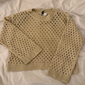 Beige stickad tröja med hålmönster - Säljer en beige stickad tröja från H&M med snyggt hålmönster över hela plagget. Tröjan har rund halsringning, långa ärmar och ribbade muddar. Perfekt för lager-på-lager och ger en chill vibe till din outfit.