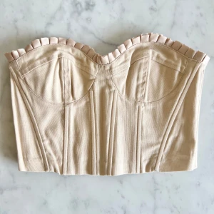 Bustiertopp med satinkant - En kort bustiertopp från H&M med dekorativ satinkant, hjärtformad ringning. Toppen har formsydda kupor samt stödskenor framtill, bak och i sidorna som ger bra stöd. Breda elastiska partier bak samt synlig dragkedja. Ofodrad. Perfekt för att skapa en trendig look med hög midja eller kjol. Toppen är i ett fint skick med några få lösa trådar på satinkanten. Om du har frågor så tveka inte på att skriva, jag finns här för att hjälpa dig. 💁🏼‍♀️