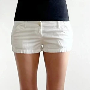 Vita shorts med fickor - Snygga vita shorts med klassisk passform och fickor fram. De har en enkel design med knapp och dragkedja framtill, perfekta för varma dagar. Shortsen är i ett lätt material som känns skönt mot huden och passar till många olika stilar.