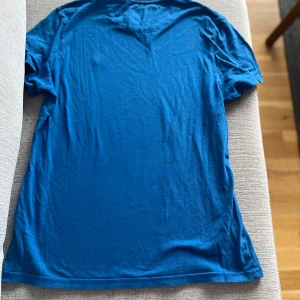 Blå t-shirt från Lyle & Scott - Snygg blå t-shirt från Lyle & Scott i ekologisk bomull. Klassisk passform med korta ärmar och rund hals. På bröstet sitter den ikoniska gula loggan som ger en clean och stilren look. Perfekt för dig som gillar enkel och tidlös stil.