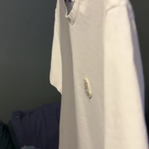 Vit Moncler t-shirt i bomull - Snygg vit t-shirt från Moncler med klassisk rund hals och korta ärmar. På bröstet sitter Monclers ikoniska logotyp. T-shirten är i mjuk bomull och har en clean, stilren look som passar perfekt till jeans eller shorts.