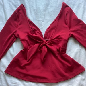 Tie Back LS Top - Röd topp med lång ärm, djup v-ringning och snygg knytning backtill. Nyköpt från Nelly och har aldrig används av mig, däremot utan prislapp!💓