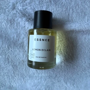 ESSNCE Lemon Eclair Eau de Parfum - Fräsch parfym från ESSNCE med doften Lemon Eclair. Flaskan är rund i genomskinligt glas med svart lock och vit etikett. Innehållet är ljusgult och designen är stilren och modern. Perfekt för dig som gillar citrus och söta toner.  ENDAST TESTAD. 