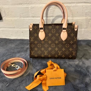 Louis Vuitton Monogram handväska - Säljer en ikonisk handväska från Louis Vuitton i klassiskt monogrammönster. Väskan är brun med ljusa handtag och detaljer, har röd insida och guldiga metalldetaljer. Kommer med axelrem och Louis Vuitton-dustbag. Perfekt storlek för det viktigaste.