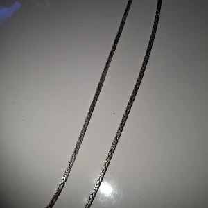 Silverfärgat halsband i kedjemodell - Säljer ett stilrent halsband i silverfärg med snyggt kedjemönster. Halsbandet har en klassisk karbinhake och är märkt med 925, vilket indikerar äkta silver. Perfekt accessoar för att lyfta din outfit.