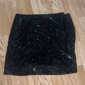 Svart paljettkjol - Säljer en svart minikjol täckt med glittrande paljetter. Kjolen har en rak och tajt passform. Den är kort och passar storlek xs/s men det står M i plagget. Skriv för fler bilder!