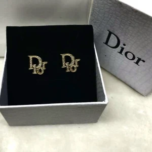 Guldiga örhängen från Dior - Säljer ett par exklusiva örhängen från Dior i guldton med glittriga stenar som formar märkets ikoniska logotyp. Perfekta för att lyfta din stil med en lyxig touch.