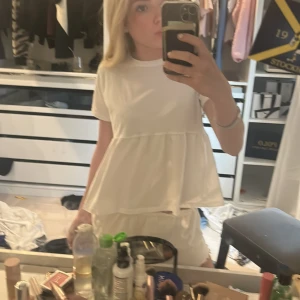 Vit tröja från lager  - Supersöt vit tröja från lager 157 med volang nedtill och korta ärmar. Den har en avslappnad passform och är gjord i mjuk bomull, perfekt för varma dagar. Enkel och stilren design som är lätt att matcha med accessoarer.