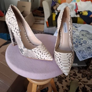 Ormskinnsmönstrade pumps från Steve Madden - Säljer ett par snygga pumps från Steve Madden med ormskinnsmönster i beige och svart. Skorna har spetsig tå och hög, bred klack som ger extra stabilitet. Perfekta för dig som vill sticka ut med ett djurmönster.