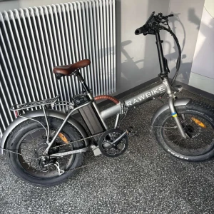RAWBIKE 3x 750watt  elcykel med breda däck - Säljer en RAWBIKE elcykel i grått med breda svarta däck och brunt sadel. Cykeln har digital display, pakethållare bak och hopfällbar ram. Perfekt för både stad och terräng. Batteriet sitter under sadeln och cykeln har robusta detaljer. 